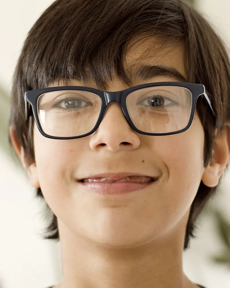 Menino de óculos de armação escura sorrindo (foto ilustrativa)