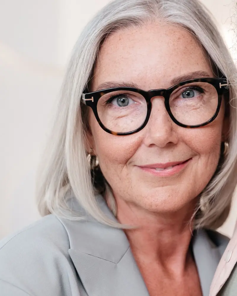 Mulher de cabelo grisalho e óculos de armação escura sorrindo (foto ilustrativa)